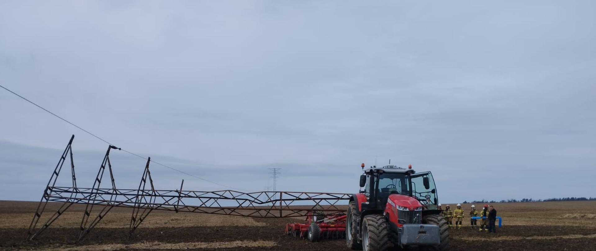 na polu rolniczym stoi traktor na którym leży przewrócony metalowy słup energetyczny
