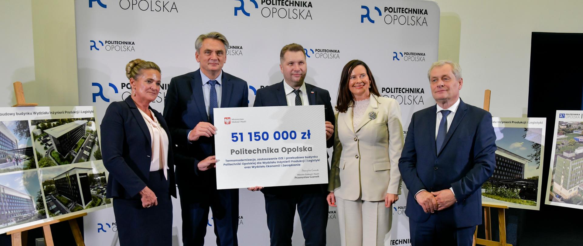 Minister Czarnek w otoczeniu czterech osób stoi na tle ściany z napisem Politechnika Opolska, trzyma duży symboliczny czek z napisem 51 150 000 zł.