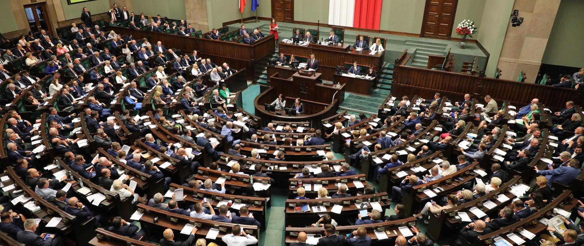 Sala plenarna Sejmu, w głębi na podwyższeniu siedzą marszałkowie, z tyłu flagi - polska i unijna
