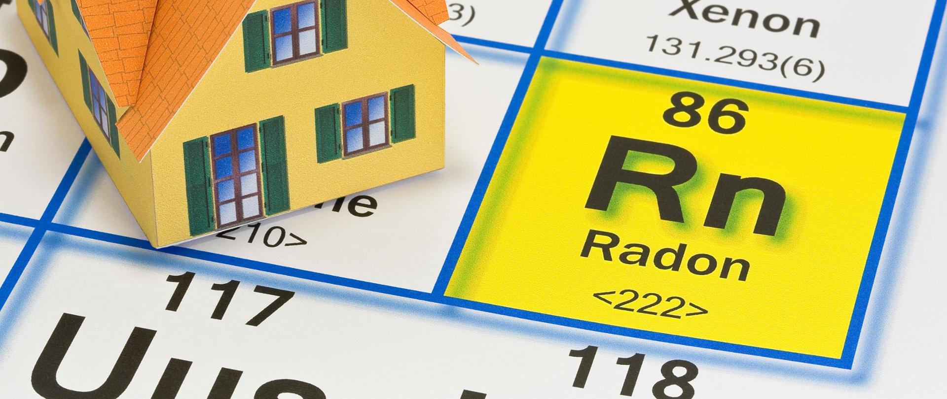 Powiększony fragment układu okresowego pierwiastków ze zbliżeniem na symbol chemiczny radonu - Rn. Obok rysunek domu jednorodzinnego.