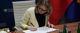 Wiceminister funduszy i polityki regionalnej Monika Sikora podczas podpisywania umowy na wsparcie inkubatorów na innowacje społeczne, wiceminister siedzi przy stole i podpisuje dokument