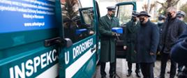 Po lewej stronie stoi z otwartymi drzwiami nowy pojazd służbowy typu furgon ITD Radom. Radiowóz i jego specjalistyczne wyposażenie prezentuje Mazowiecki Wojewódzki Inspektor Transportu Drogowego Krzysztof Chojnacki i jego zastępca Zbigniew Kapciak.