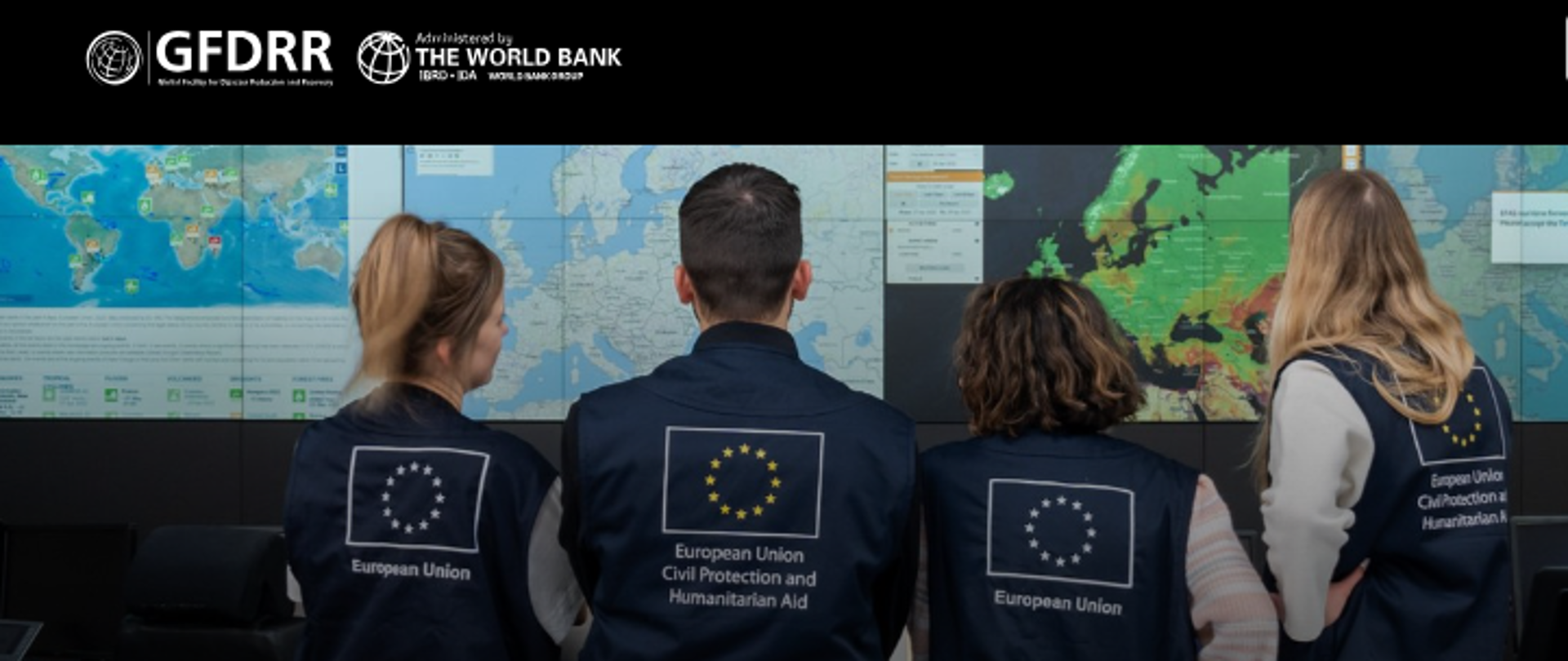 cztery osoby stoją tyłem na tle monitorów z mapami, na plecach na kamizelce mają napis European Union