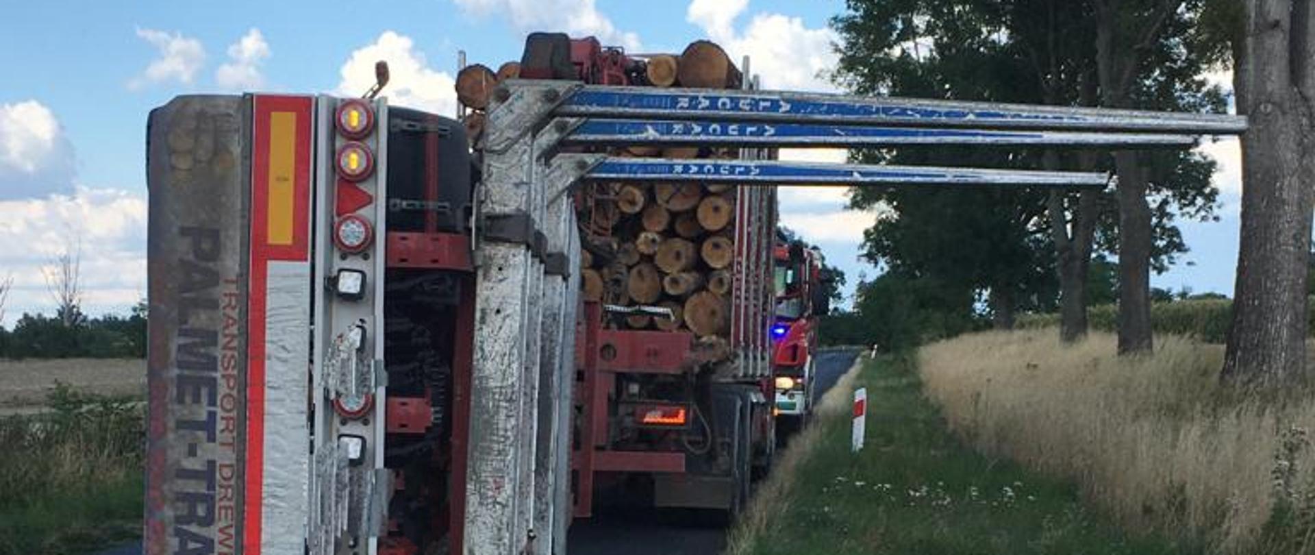 Wypadek z udziałem samochodu przewożącego drzewo na DW 462 w pobliżu Łosiowa - zdjęcie przedstawia położoną na boku pustą przyczepę, przed nią stoi samochód ciężarowy wypełniony drzewem