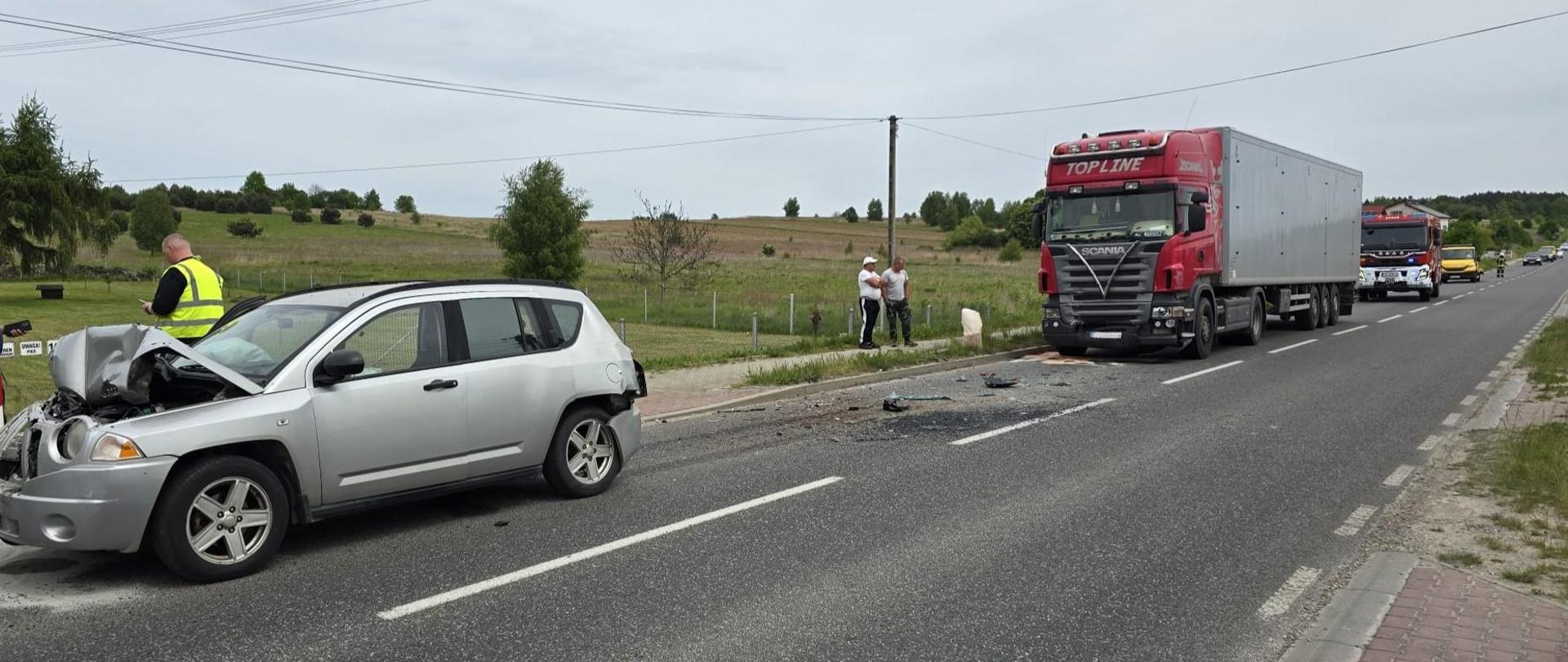 Zdjęcie przedstawia drogę wojewódzką. Po lewej samochód osobowy po zderzeniu z ciężarówka i busem, po prawej ciężarówka uczestnicząca w wypadku komunikacyjnym