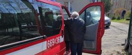 Na zdjęciu starsza osoba wchodzi do samochodu pożarniczego
