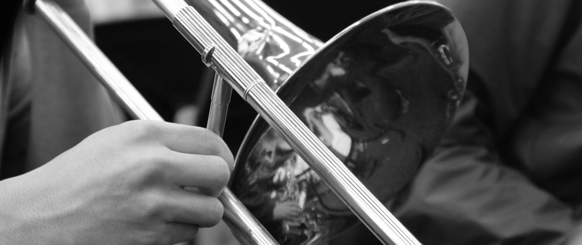 czarno-biała fotografia przedstawiająca czarę puzonu oraz dłoń trzymającą instrument