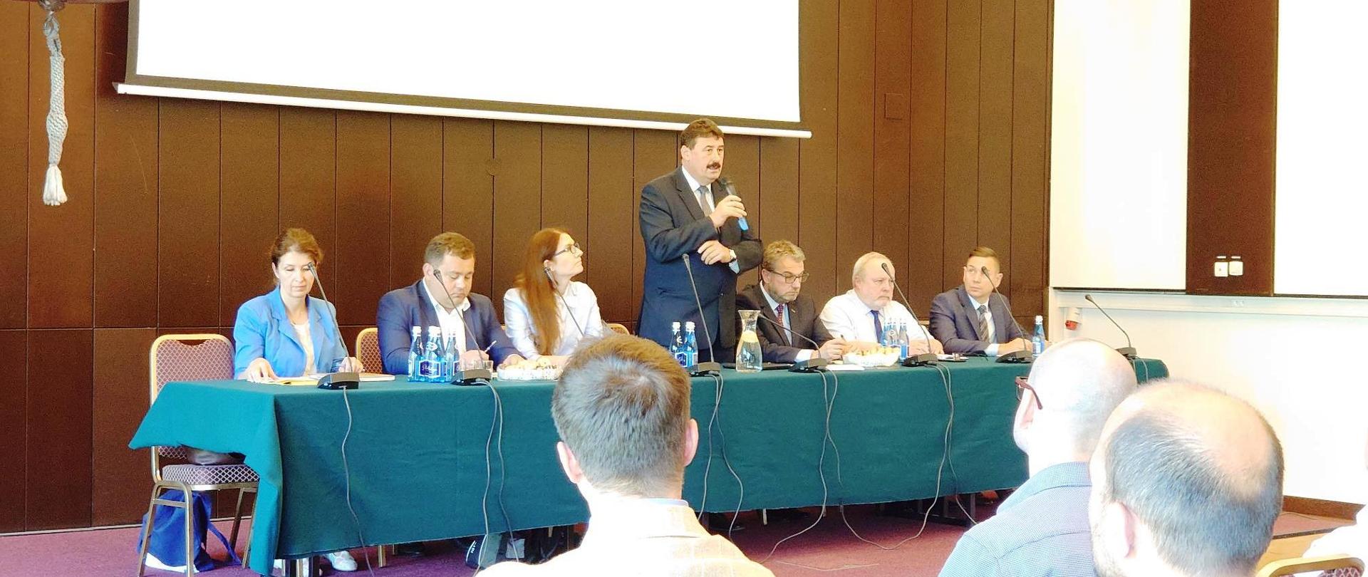 Sekretarz stanu Ryszard Bartosik przemawiający do mikrofonu stojąc za stołem prezydialnym.