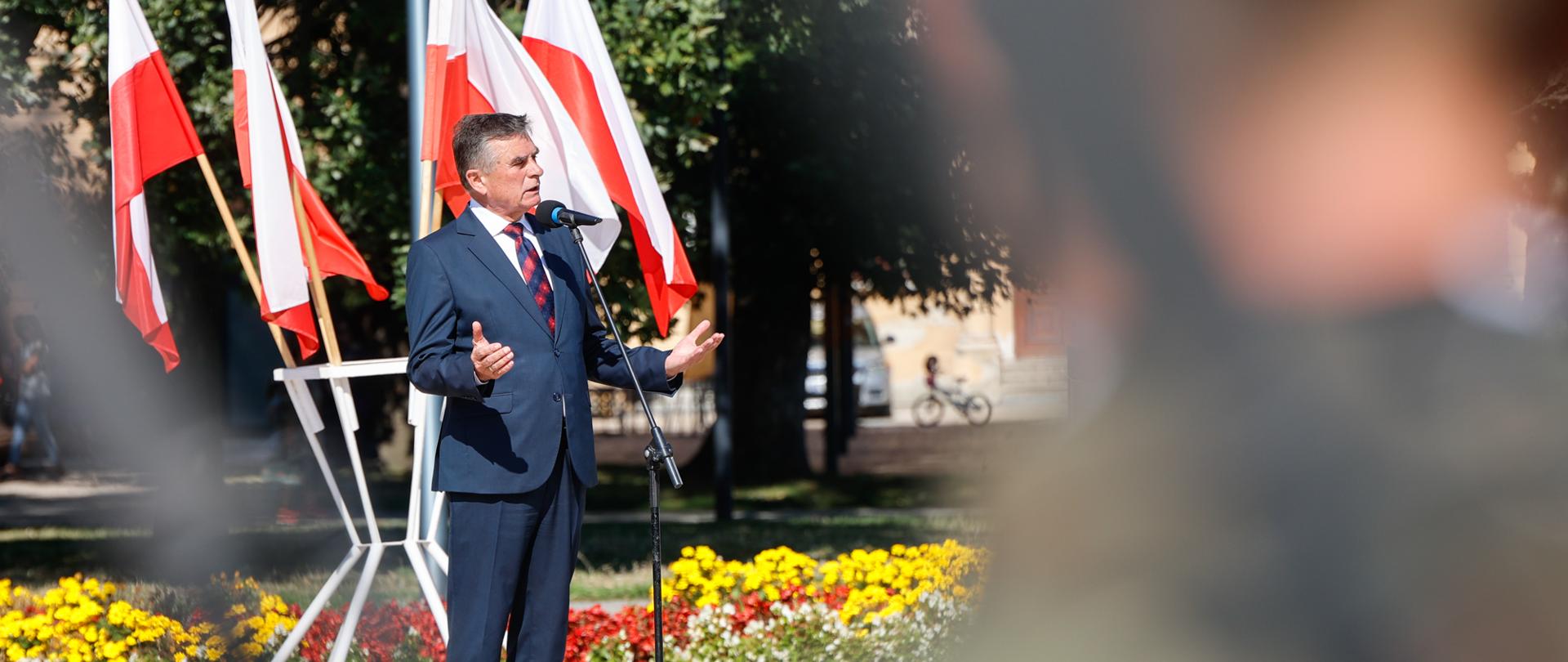 Wojewoda lubelski przemawia. W tle flagi polskie i kwiaty.