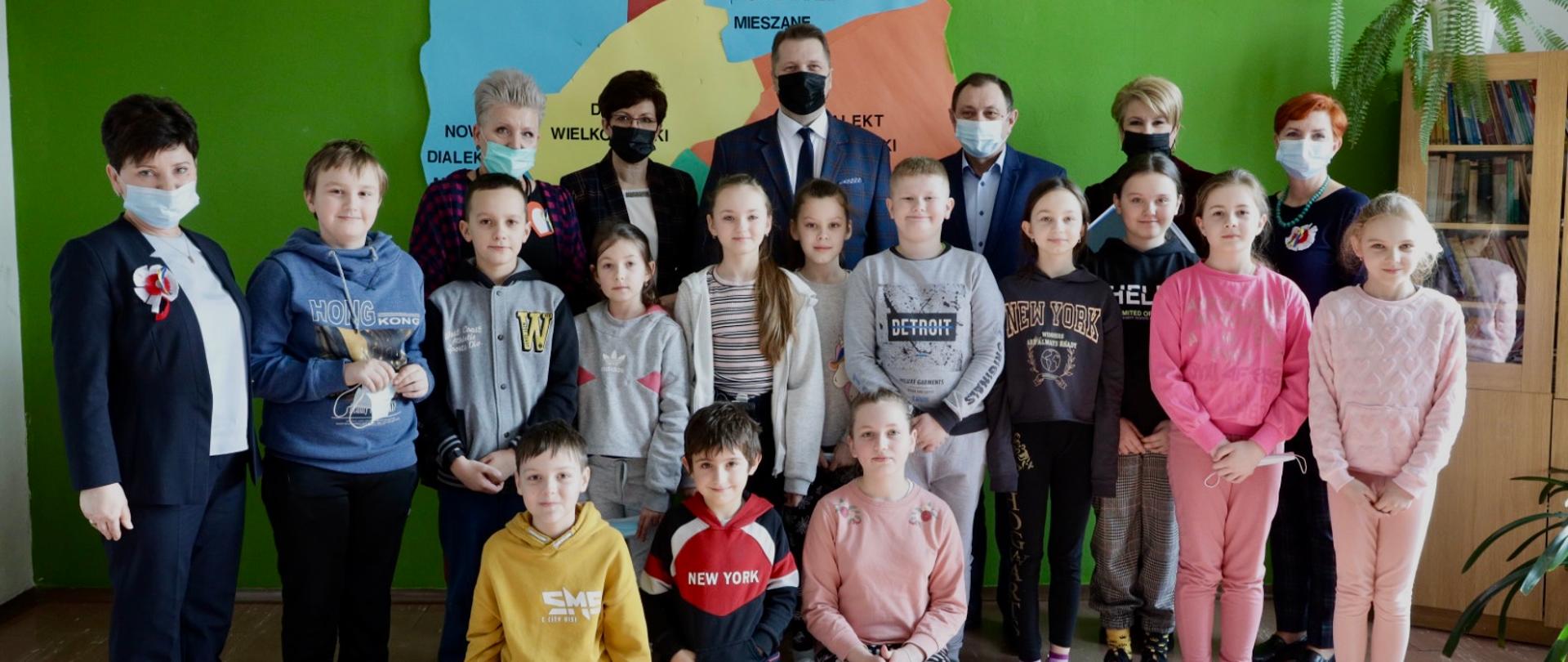 Minister Przemysław Czarnek pozuje do zdjęcia z uczniami i nauczycielami ze szkoły w Horodle. Za nimi wisi mapa Polski.