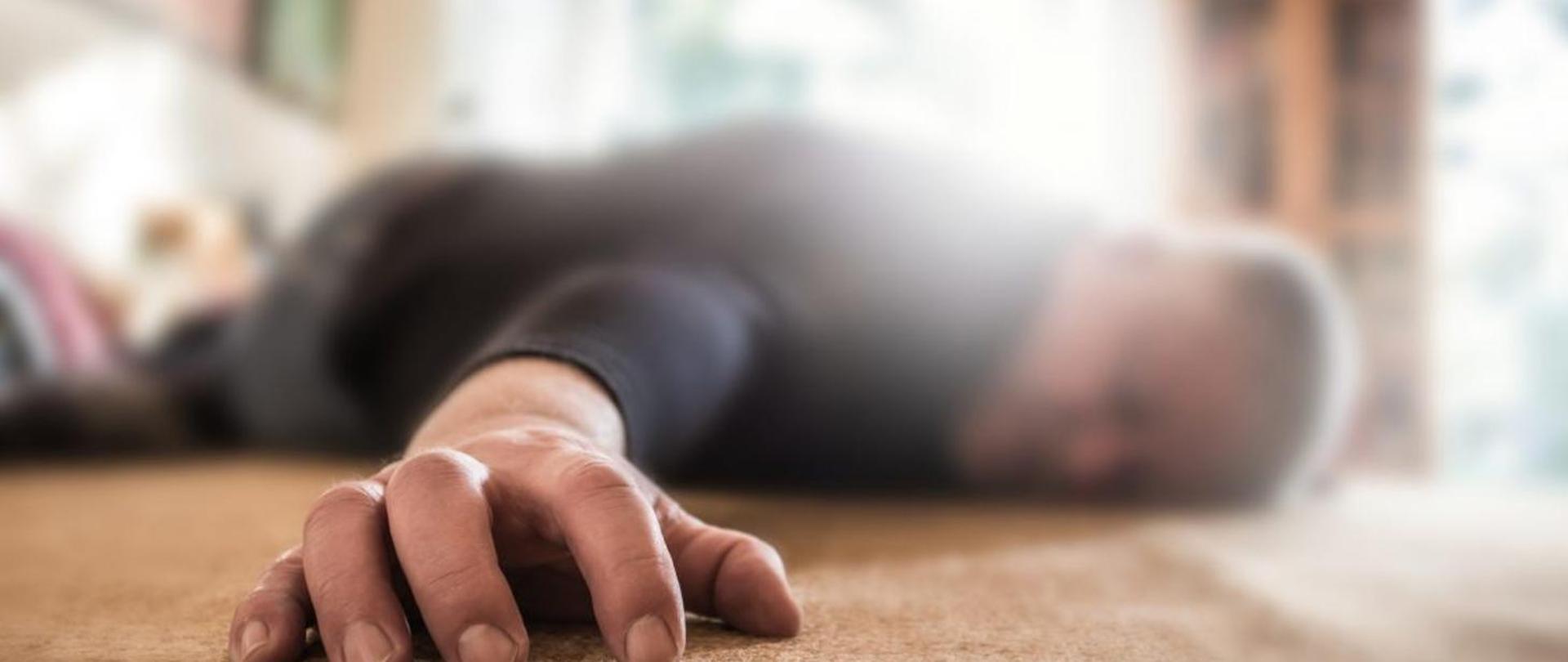 Człowiek - mężczyzna leżący na podłodze, z przodu zdjęcia leżąca jego dłoń