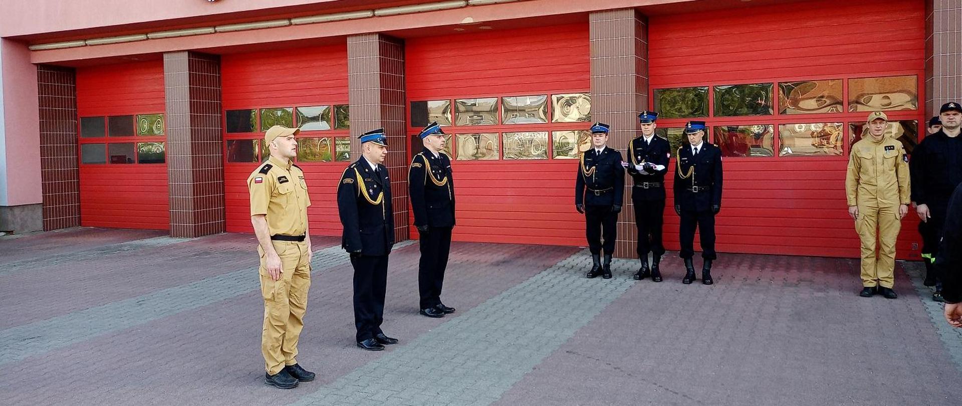 Strażacy w mundurach wyjściowych i służbowych stoją na baczność.