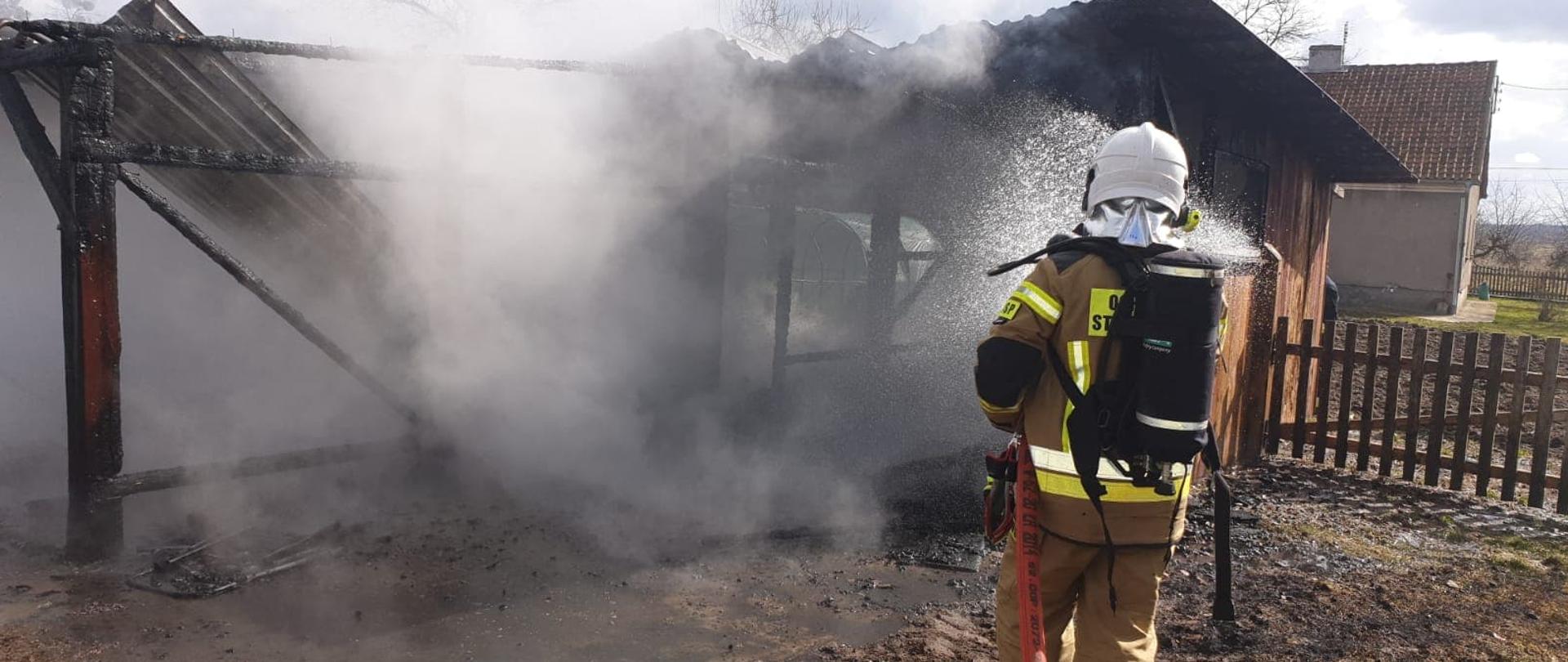 Na zdjęciu widać strażaka dogaszającego pożar garażu, który w ręku trzyma wąż strażacki