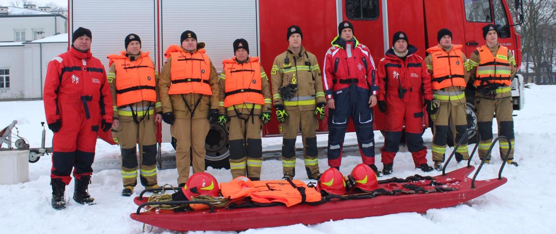 Pokaz ratownictwa wodno-lodowego w ramach akcji „Bezpieczne ferie” 18.01.2024 r. - na zdjęciu członkowie grupy stoją przed samochodem na śniegu.