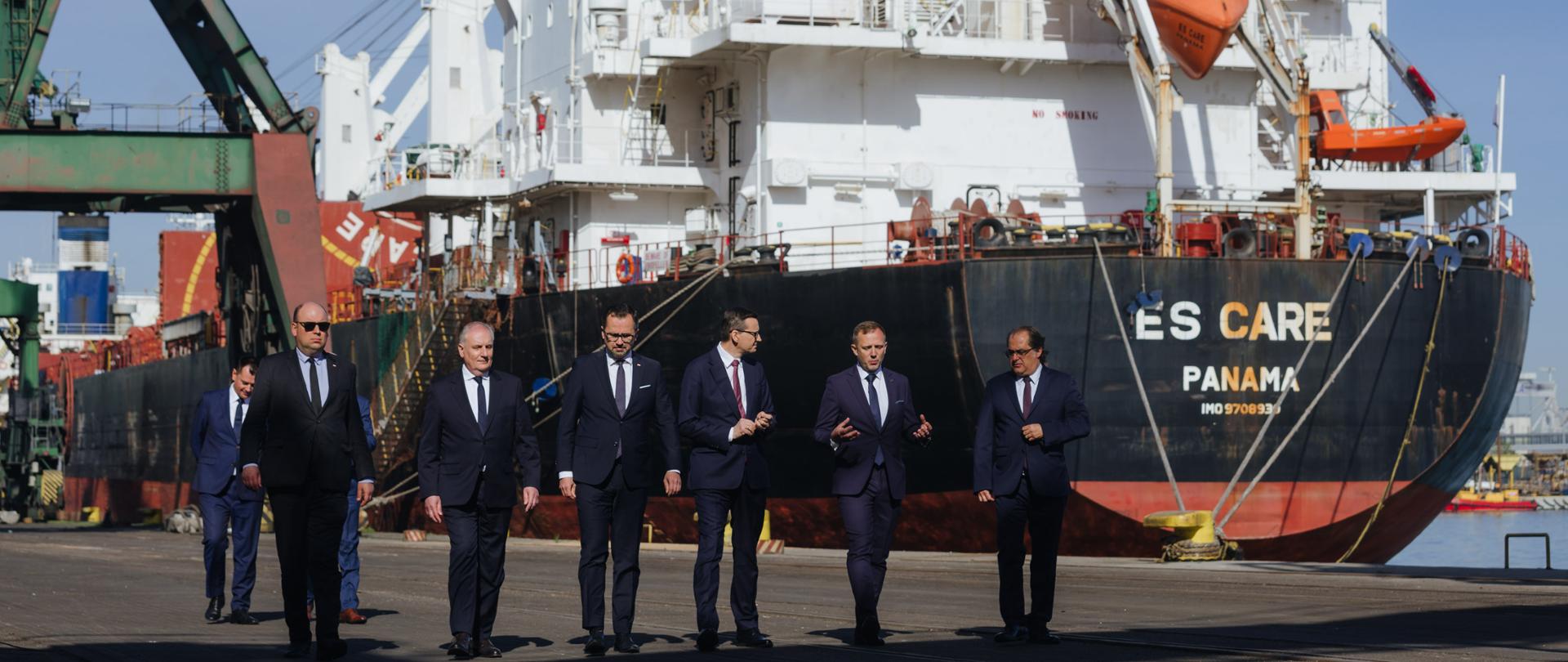 Premier oraz delegacja idą na tle statku.