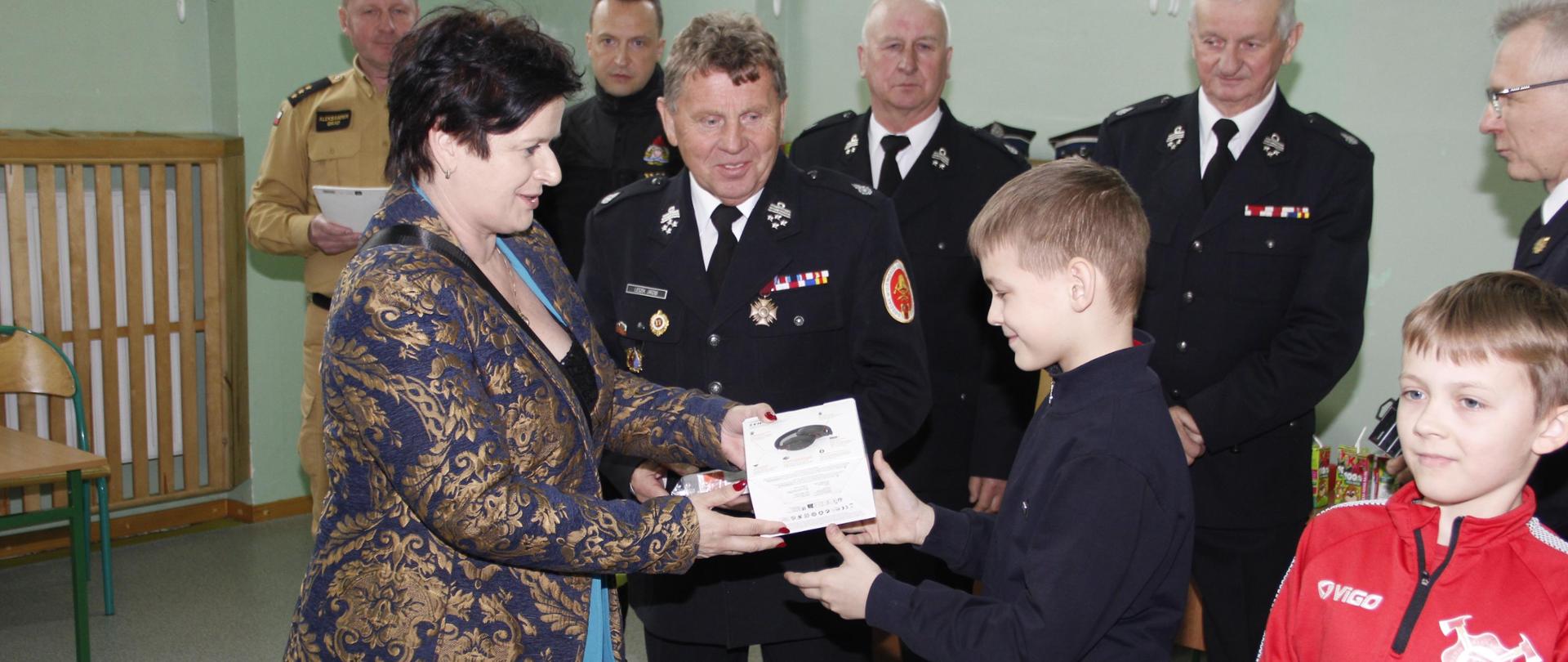 Wręczenie nagród najmłodszym uczestnikom turnieju, nagrodę dwojgu dzieci wręcza starosta brzeziński pani Renata Kobiera. w tle organizatorzy oraz prezesi OSP.