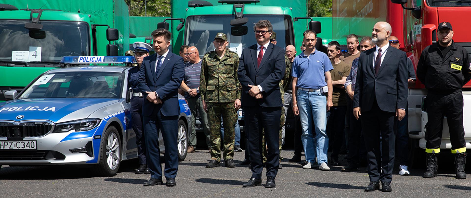 Na zdjęciu Minister Michał Dworczyk oraz wiceministrowie Maciej Wąsik oraz Maciej Lang (MSZ). W tle część konwoju z pomocą humanitarną