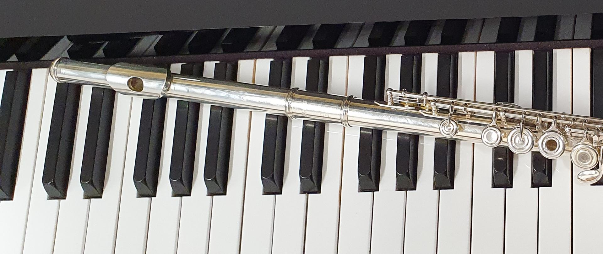 zdjęcie przedstawia flet, który umieszczony został na klawiaturze fortepianu.
