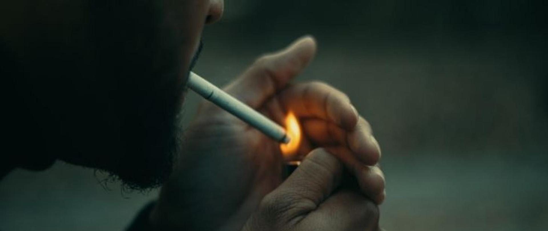 Twarz mężczyzny z papierosem, który zapala papierosa zapalniczką.