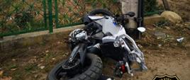 srebrny motocykl po wypadku leżący przy ogrodzeniu posesji