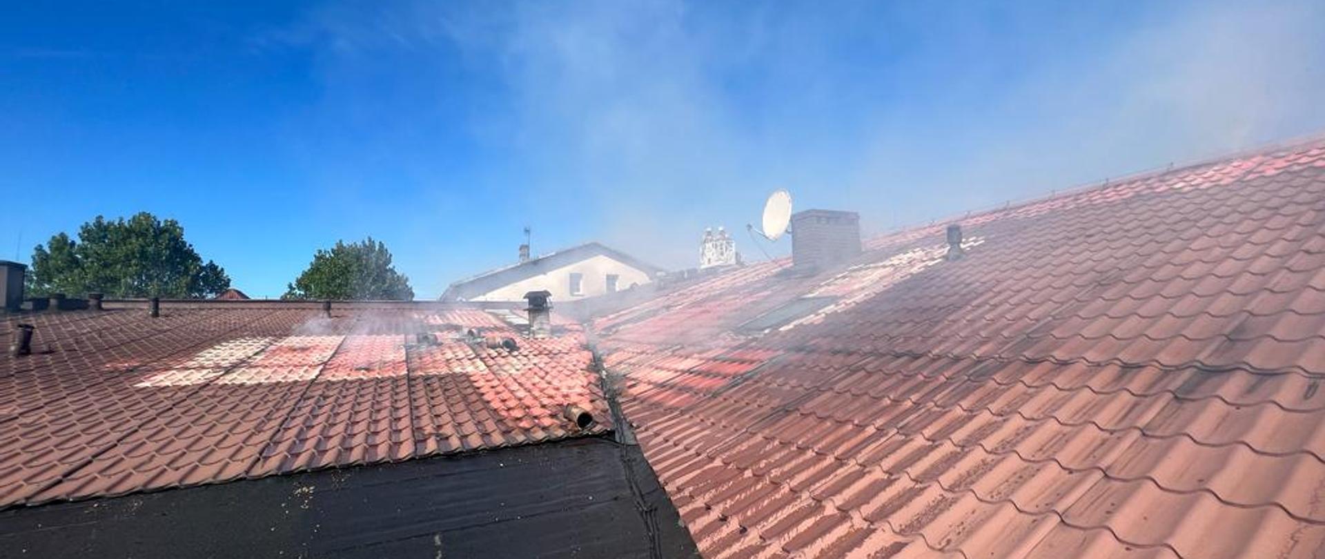 Dach z czerwonej dachówki nad którym unosi się biały dym.