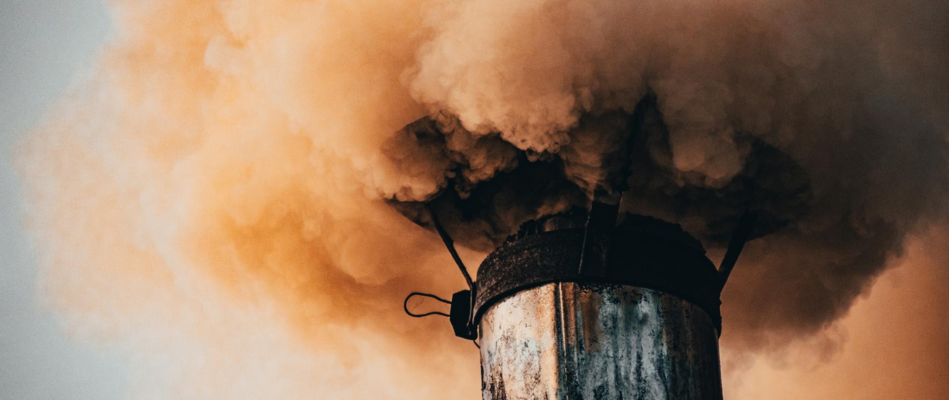 Zdjęcie przedstawia dymiący komin z żółtym dymem.