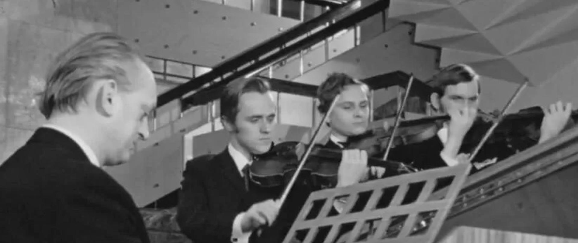 Czarno-białe zdjęcie grającego Bernarda Biagonia i towarzyszącemu mu 3 skrzypków
