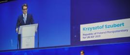 Szczyt Cyfrowy ONZ – IGF 2021. Krzysztof Szubert na scenie za mównicą. Za nim ekran. Fot. PAP