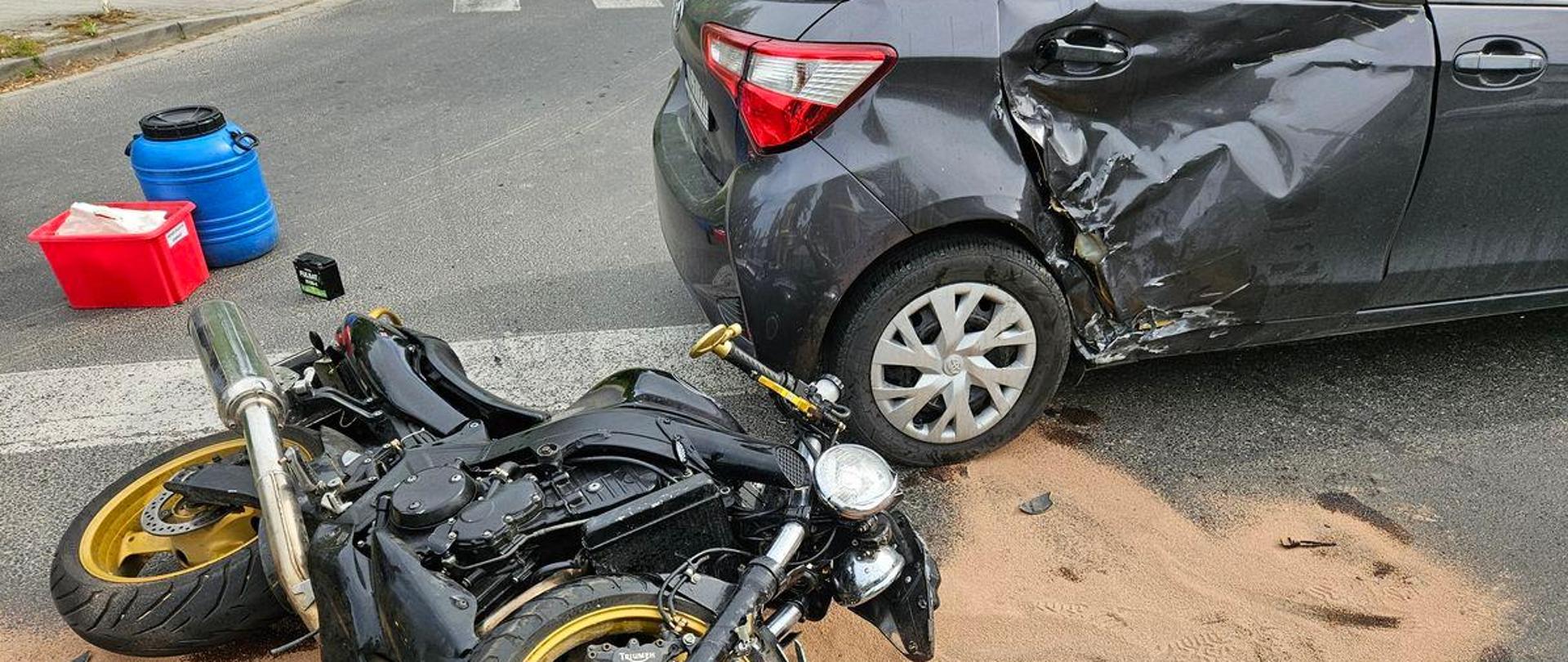 Motocykl na drodze oraz uszkodzony samochód osobowy