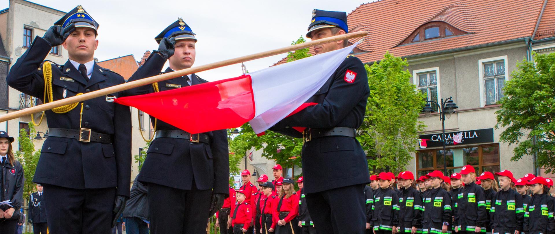 Strażacki poczet flagowy w czasie uroczystego wieszania flagi na drabinie strażackiej