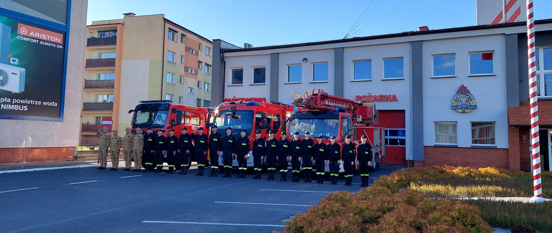 Zdjęcie ukazuje strażaków oddających hołd dla zmarłego strażaka na tle budynku komendy w Krotoszynie