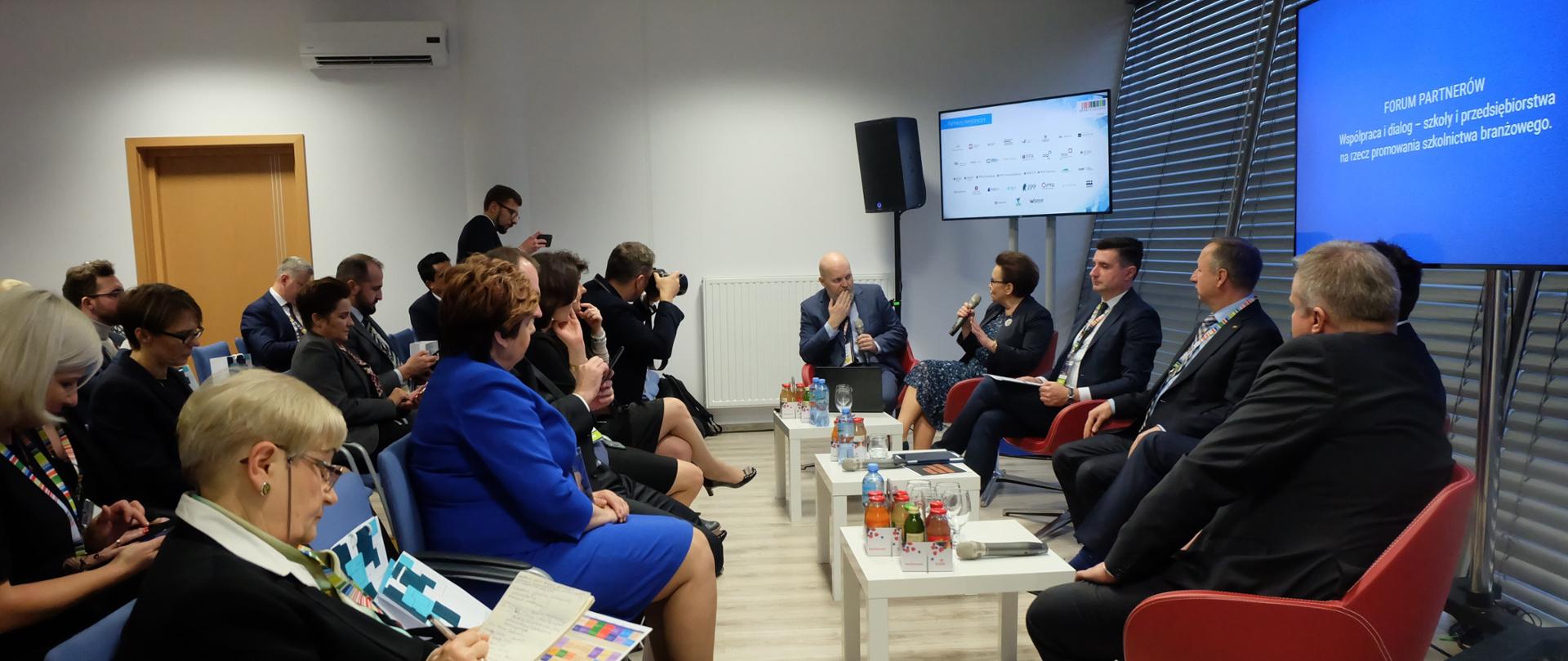 Panel dyskusyjny z udziałem minister Anny Zalewskiej. Na fotelach siedzą uczestnicy dyskusji, za nim monitory ekranowe