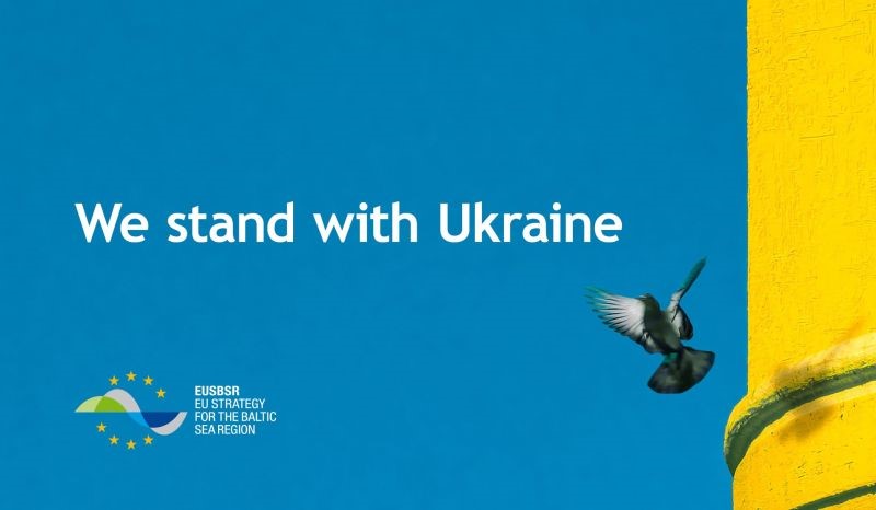 Grafika - na tle niebiesko-żółtej flagi Ukrainy mały ptaszek, obok napis We stand with Ukraine.