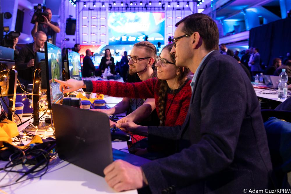 Premier Mateusz Morawiecki ogląda ekran komputera, który pokazuje mu programistka.