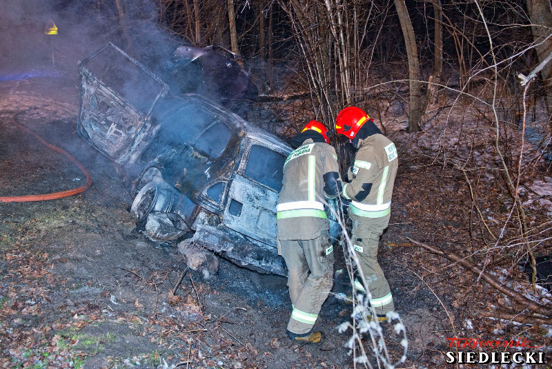 Pożar samochodu osobowego, który znajduje się w rowie obok jezdni. Na zdjęciu strażacy sprawdzający wrak pojazdu.