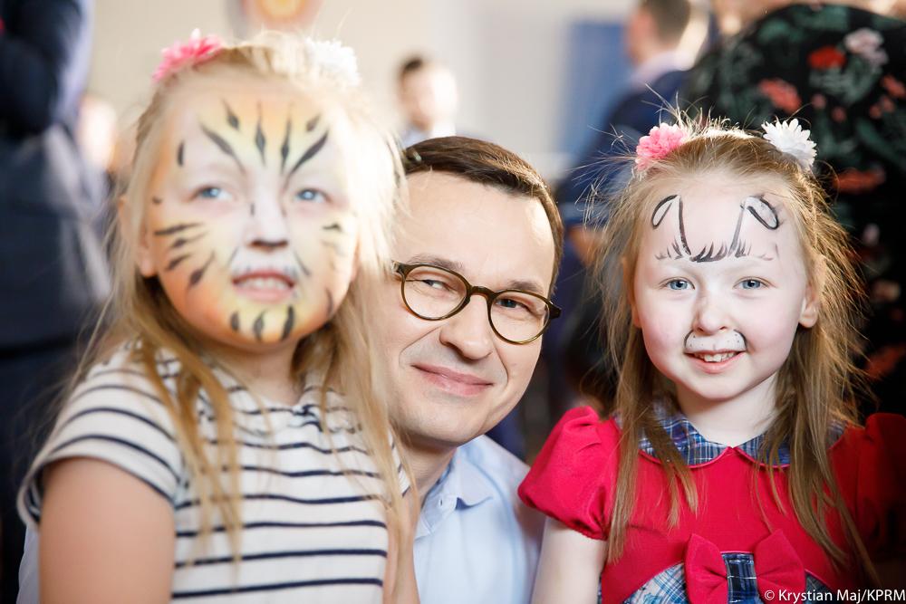 Premier Mateusz Morawiecki wraz z dziewczynkami z pomalowanymi twarzami.