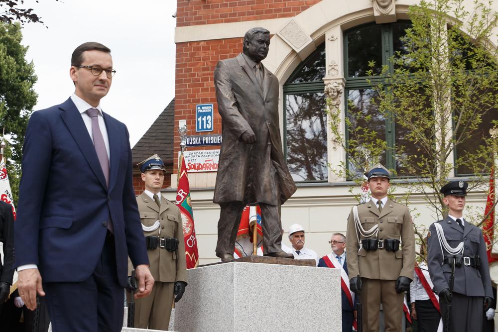 Premier Mateusz Morawiecki na tle pomnika Lecha Kaczyńskiego.