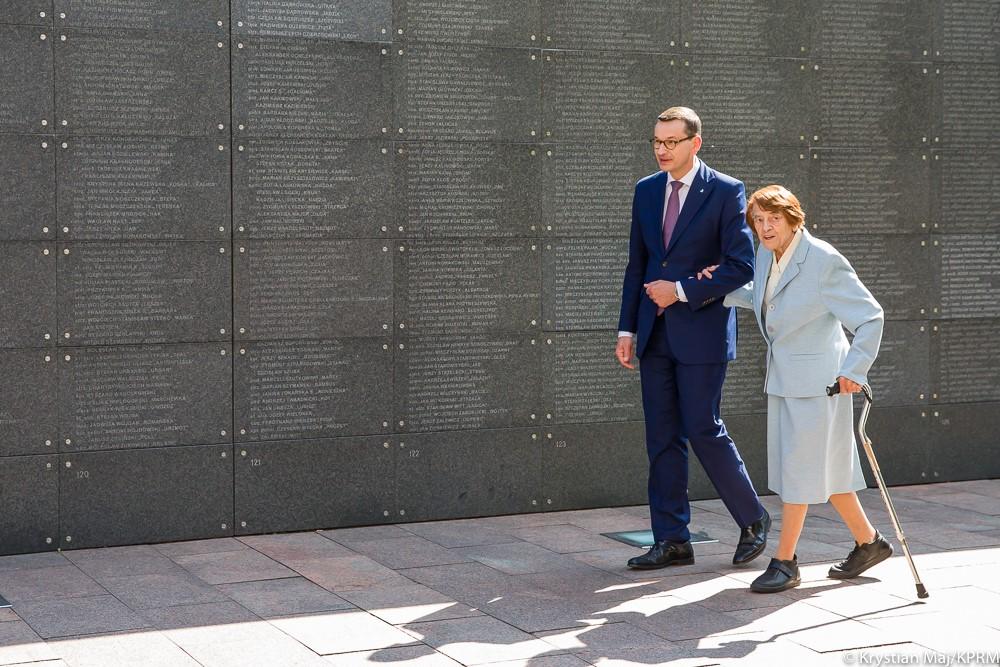 Premier Mateusz Morawiecki prowadzi pod rękę uczestniczkę powstania.