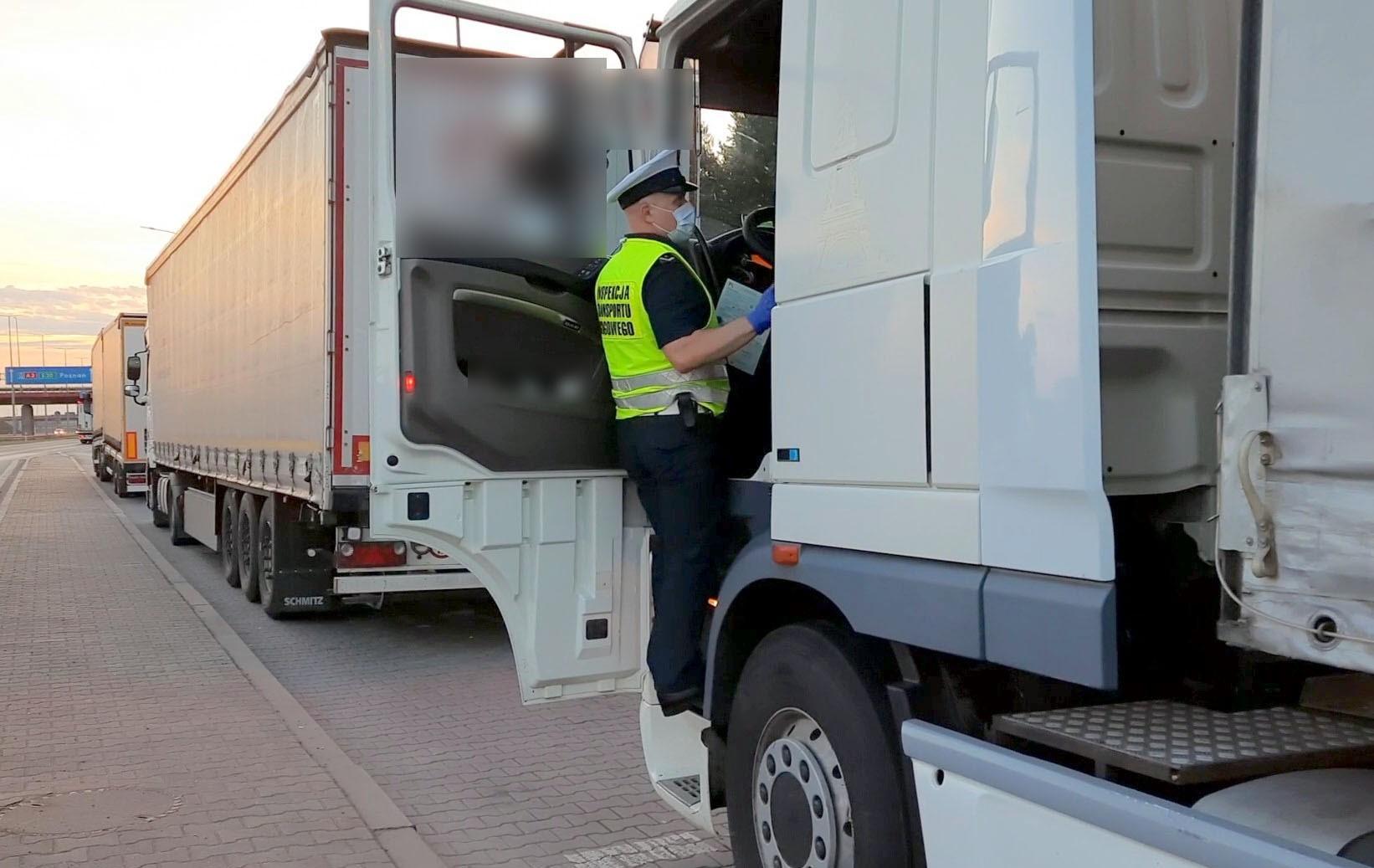 Inspektor stoi w drzwiach kabiny ciężarówki i pobiera dokumenty od kierowcy.