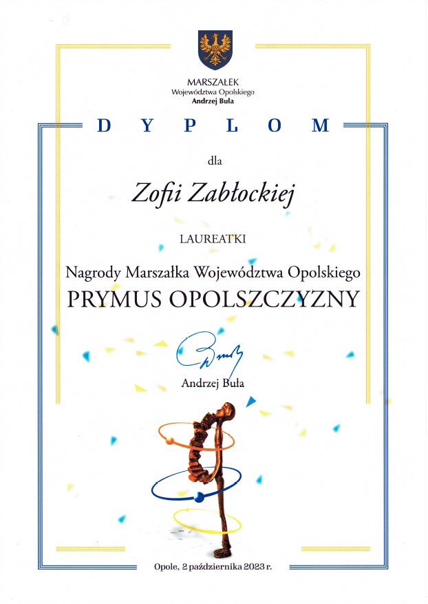 Dyplom ,białe tło, niebieska i złota ramka. U góry granatowe logo z orłem urzędu marszałkowskiego. Napis Marszałek Województwa Andrzej Buła. Dyplom dla Zofii Zabłockiej laureatki nagrody Marszałka Województwa Opolskiego Prymus Opolszczyzny. podpis nieczytelny. Poniżej Andrzej Buła. poniżej grafika statuetki w nienaturalnie wygiętej pozie z kolorowymi kołami hula-hop. Opole 2 października 2023.