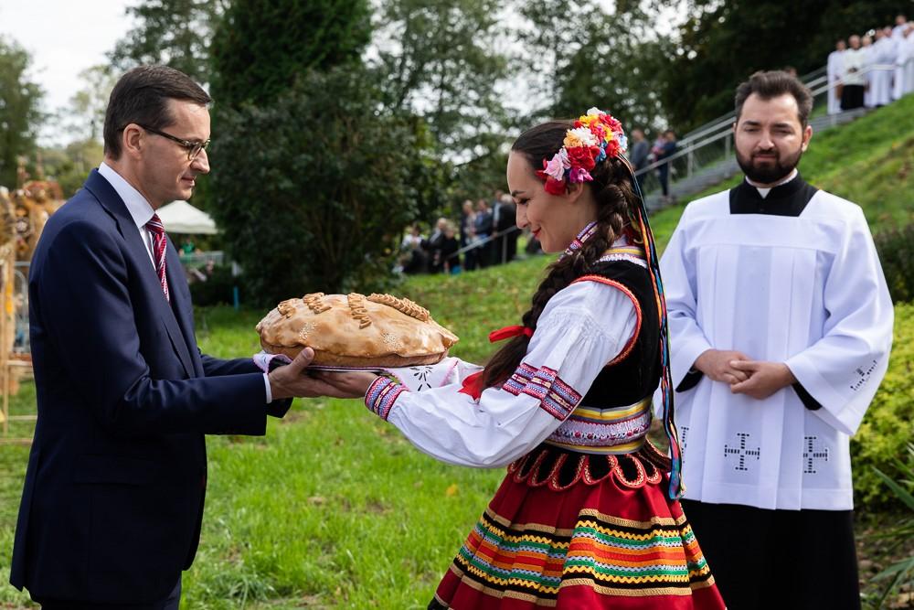 Premier Mateusz Morawiecki przyjmuje chleb od kobiety w stroju ludowym.