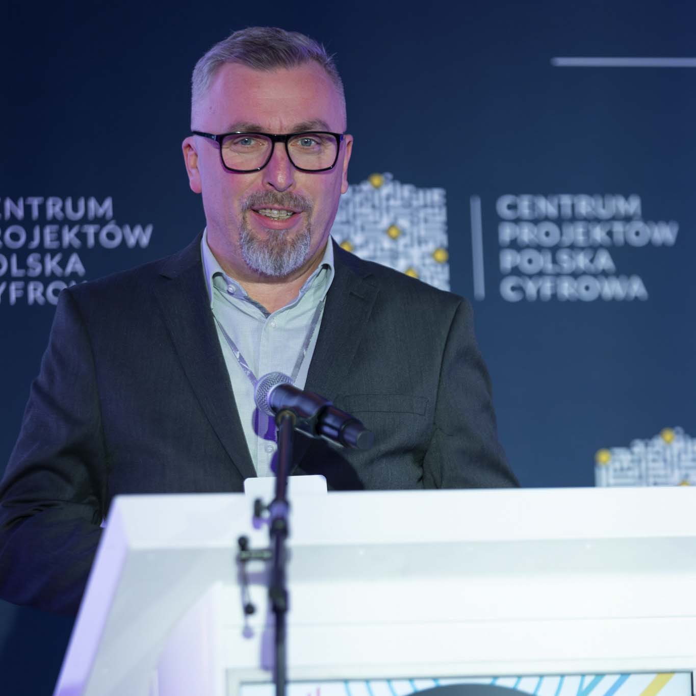 Przy mównicy stoi Pan Norbert Ogłaza. Wzrok kieruje w stronę uczetników konferencji. Mówi do mikrofonu.