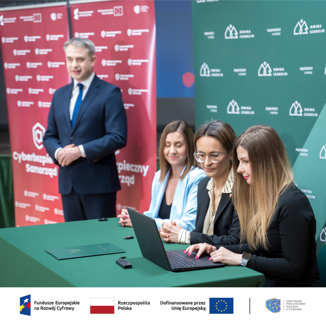 Od prawej Skarbniczka gminy Izabelin, Wójcina Gminy Izabelin oraz Dyrektor Biura Projektów Własnych CPPC podpisująca na laptopie umowę, obok Minister Cyfryzacji 