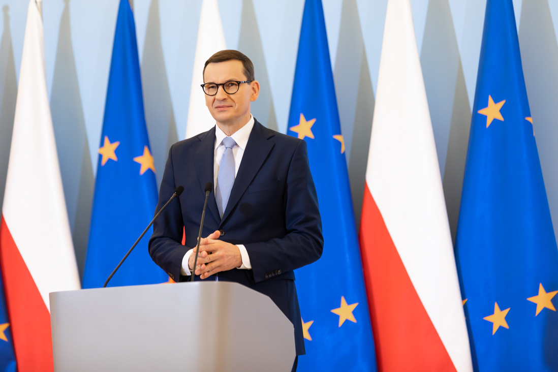 Na zdjęciu widać przemawiającego premiera Mateusza Morawieckiego na tle flag Polski i Uni Europejskiej.