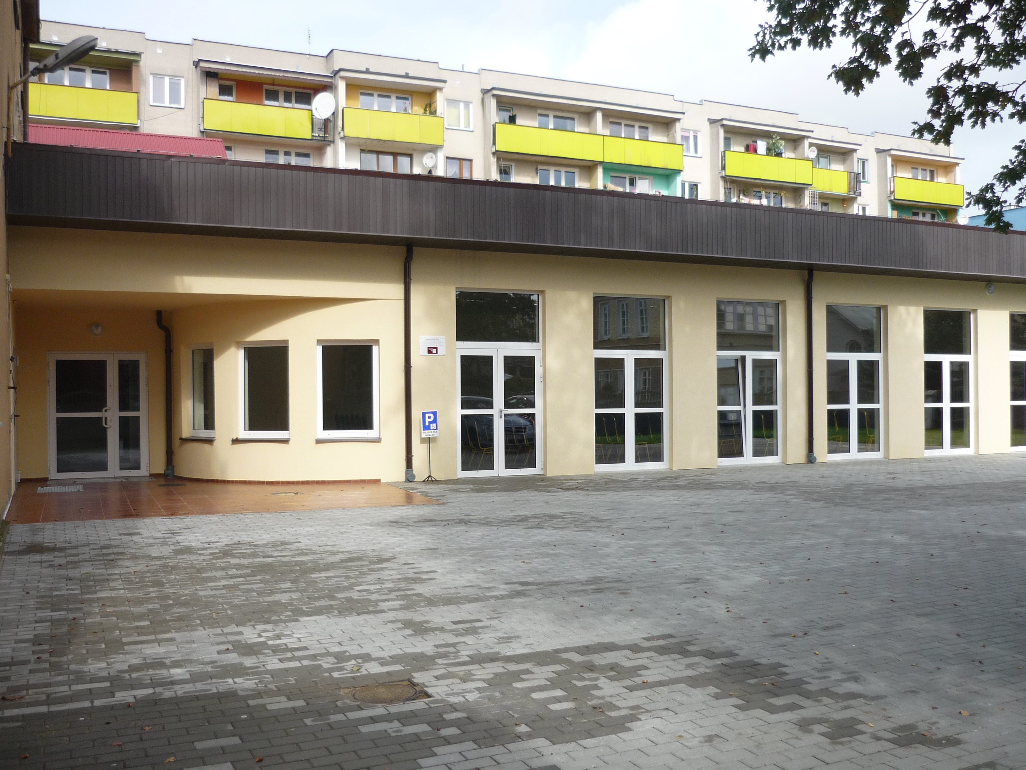 Zdjęcie przedstawia salę koncertową z zewnątrz. Budynek z jasną elewacją z licznymi oknami i wejściami 