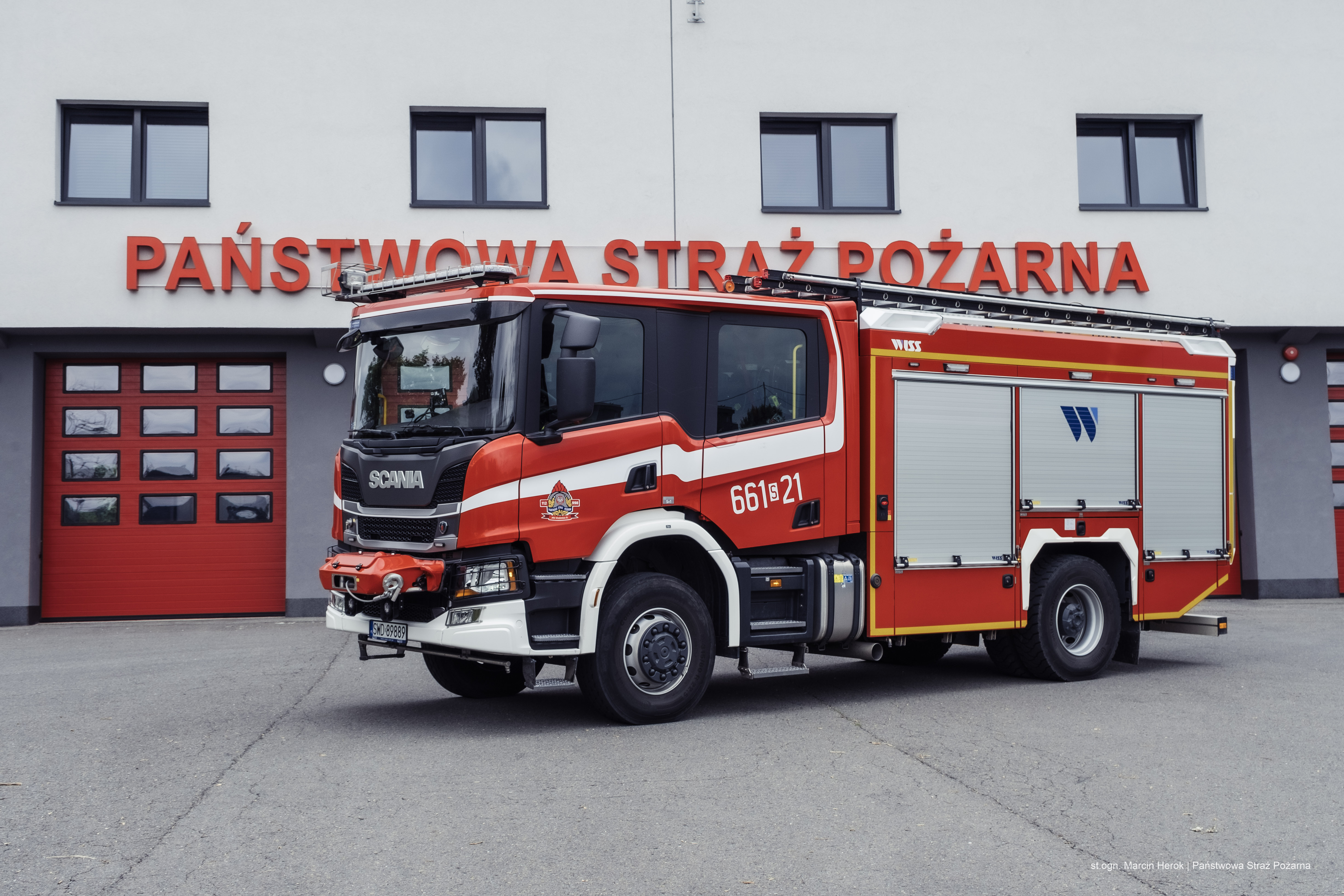 Zdjęcie przedstawia średni samochód ratowniczo-gaśniczy. W tle budynek Państwowej Straży Pożarnej