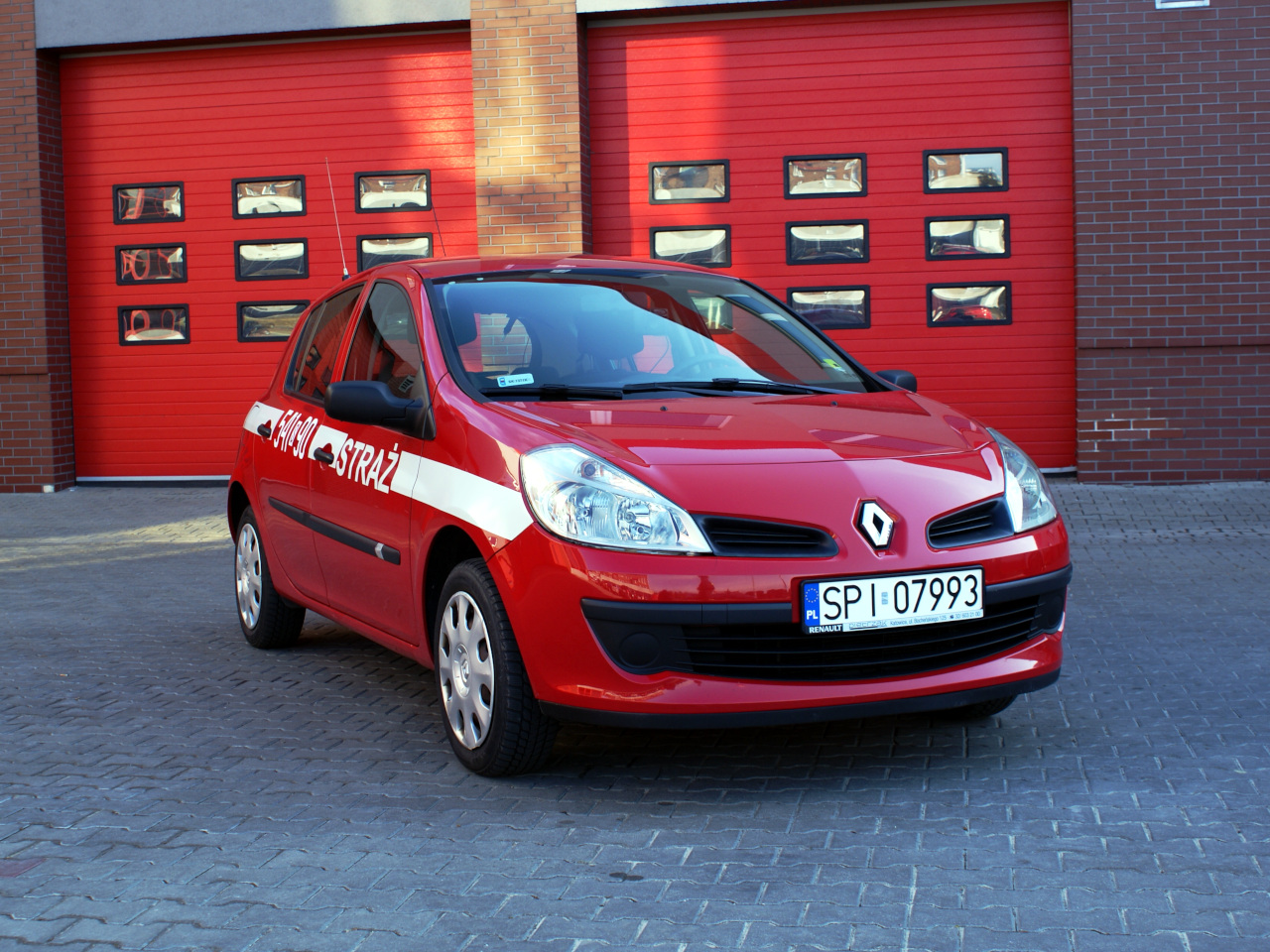 Zdjęcie przedstawia lekki samochód specjalny operacyjny marki Renault Clio w kolorze czerwonym na tle budynku komendy