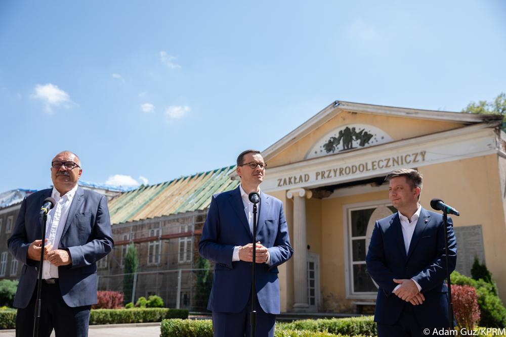 Premier Mateusz Morawiecki przemawia na tle Zakładu Przyrodoleczniczego, a obok stoi minister Michał Dworczyk.