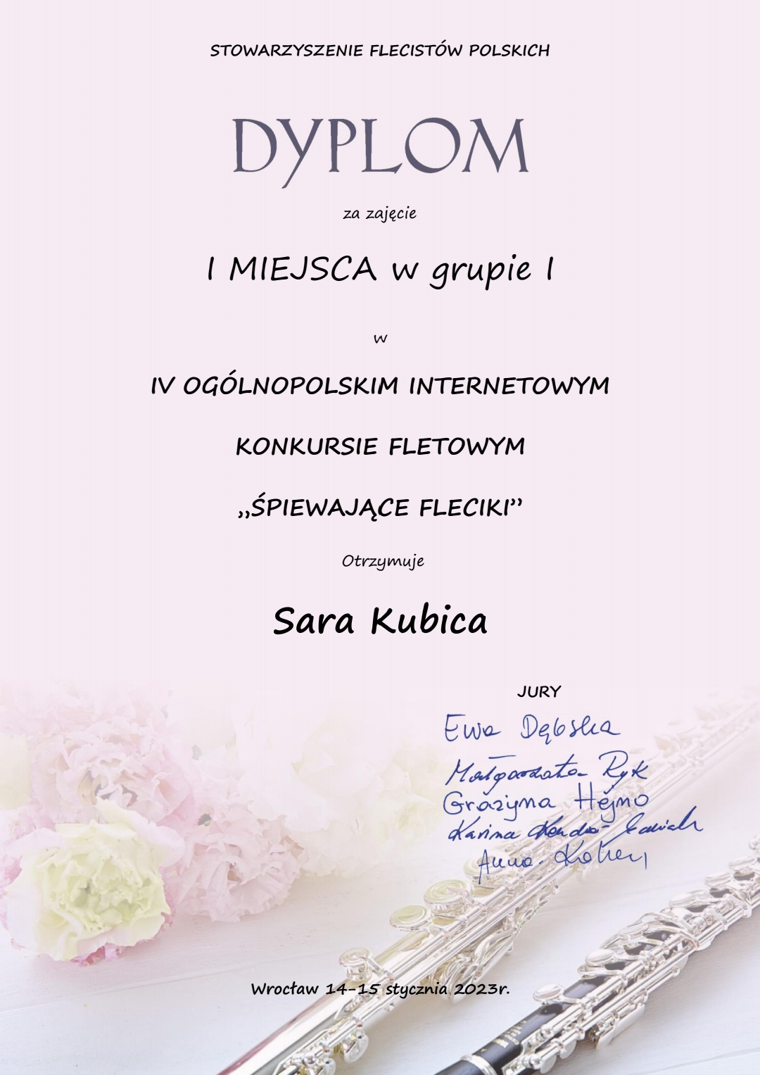 Zdjęcie dyplomu z różowym tłem, w dolnej części po lewej stronie znajduje się grafika bukietu kwiatów, po prawej stronie znajdują się dwa flety; Na dyplomie zamieszczony napis "Stowarzyszenie Flecistów Polskich, dyplom za zajęcie I miejsca w grupie I w IV Ogólnopolskim Internetowym Konkursie Fletowym "Śpiewające Fleciki" otrzymuje Sara Kubica", poniżej podpisy Jury, na dole strony napis "Wrocław 14-15 stycznia 2023 r."