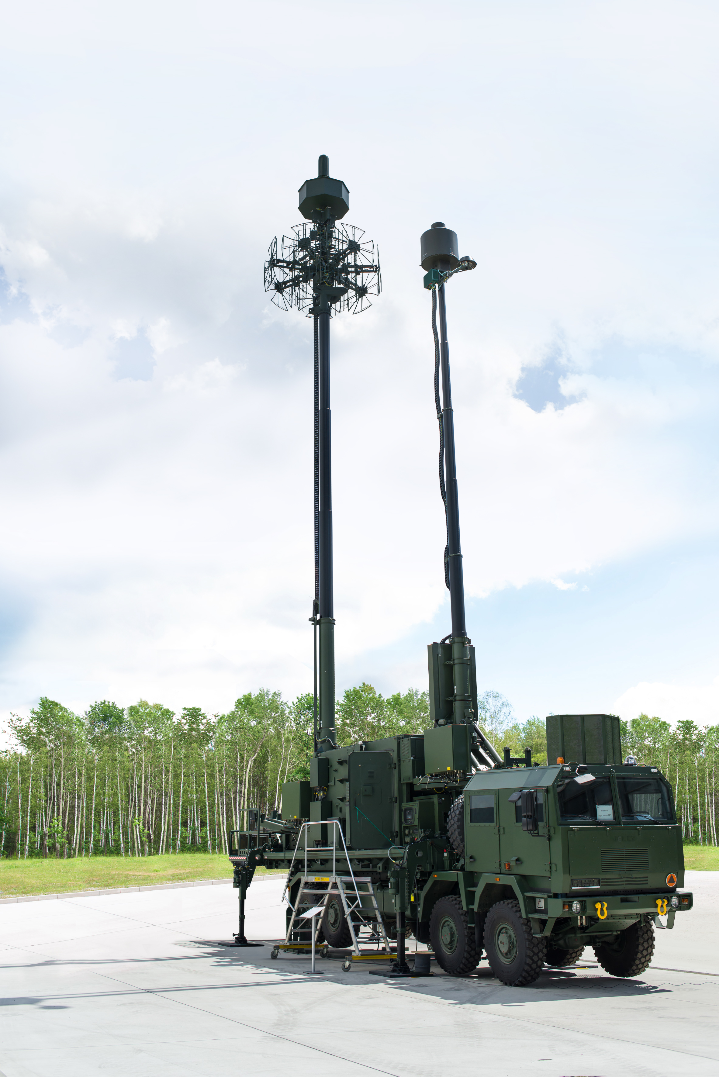 Na pierwszym planie wóz bojowy z zainstalowanym systemem pasywnej lokalizacji SPL. Wóz stoi na parkingu na poligonie. W tle las.